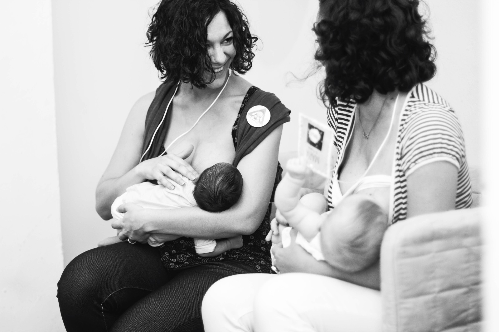 Foto en blanco y negro. Juls dando el pecho al Tritón recién nacido (1 mes) junto con María (La Furgoteta) amamantando a Olimpia. Mirada cómplice y sonrisa entre madres lactantes.
